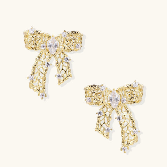 Gold-plated bow earrings with openwork design, marquise center stones, and flowing ribbon tails adorned with zirconia crystals.